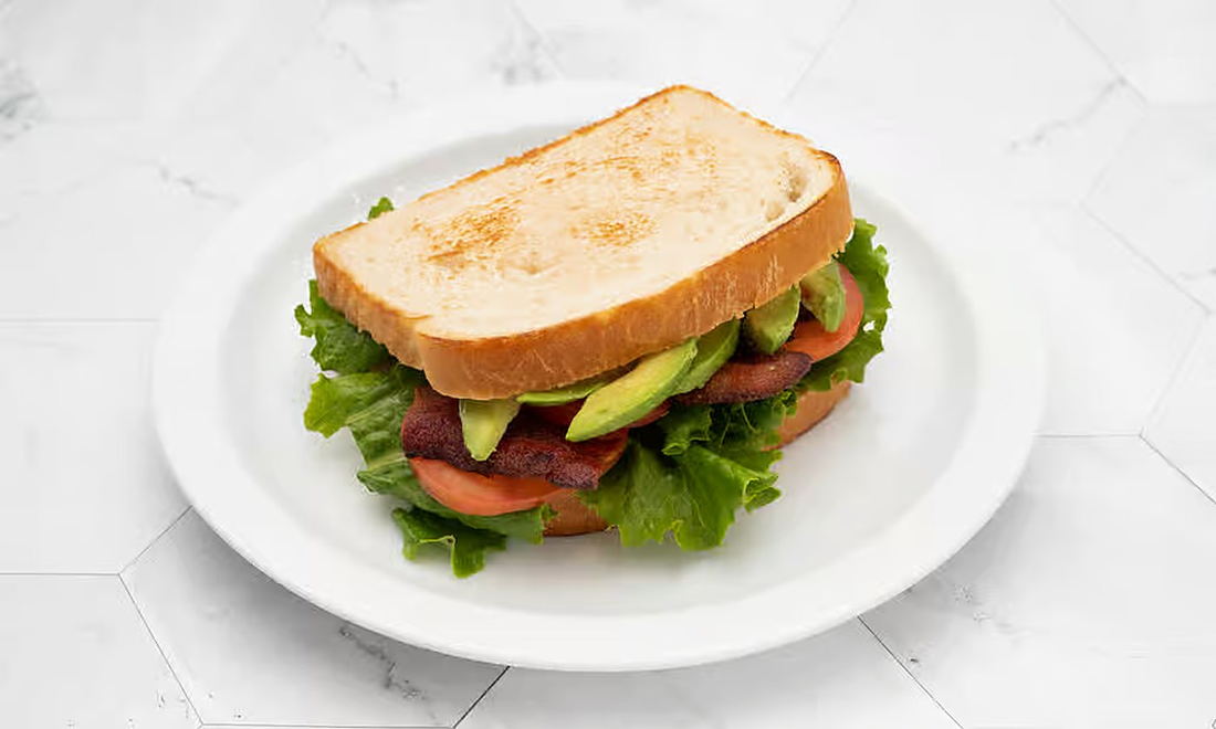 A BLT sandwich on toasted bread stacked with bacon, lettuce, tomato and sliced avocado