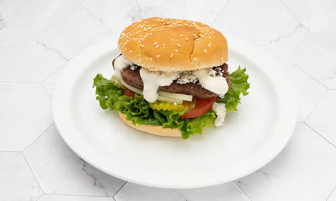 The Blue Cheeseburger — a griddled patty under blue cheese crumbles and dressing, with lettuce, tomato and onion on a sesame bun
