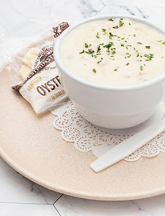 A cup of creamy clam chowder topped with herbs, served with oyster crackers