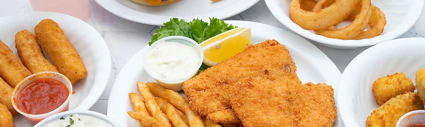 A spread of fried seafood plates — breaded fish fillets, halibut bites, onion rings, fries and dipping sauces