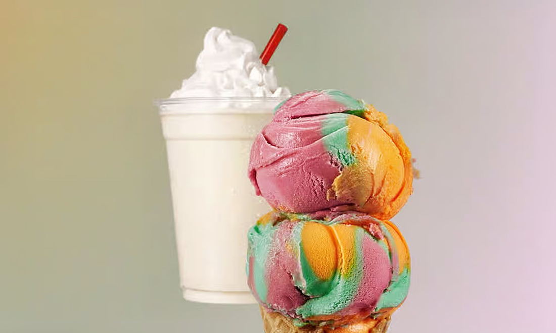 A thick vanilla milkshake with whipped cream beside a double scoop of rainbow ice cream in a cone